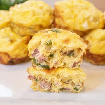 two halves of egg cups stuffed with ham, peppers, and onion stacked on a plate of other egg cups.
