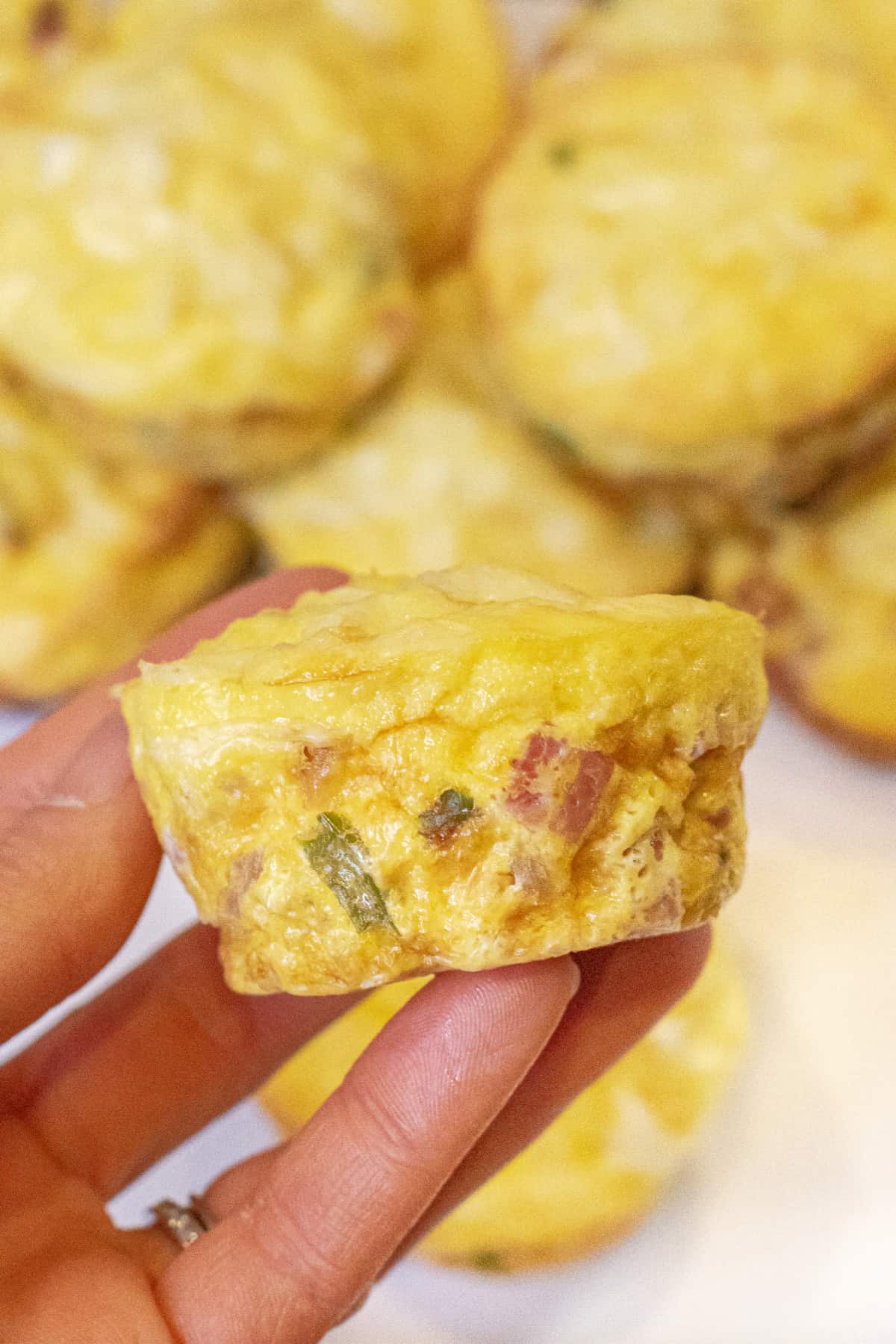 a hand holding a cooked egg cup with ham and peppers.