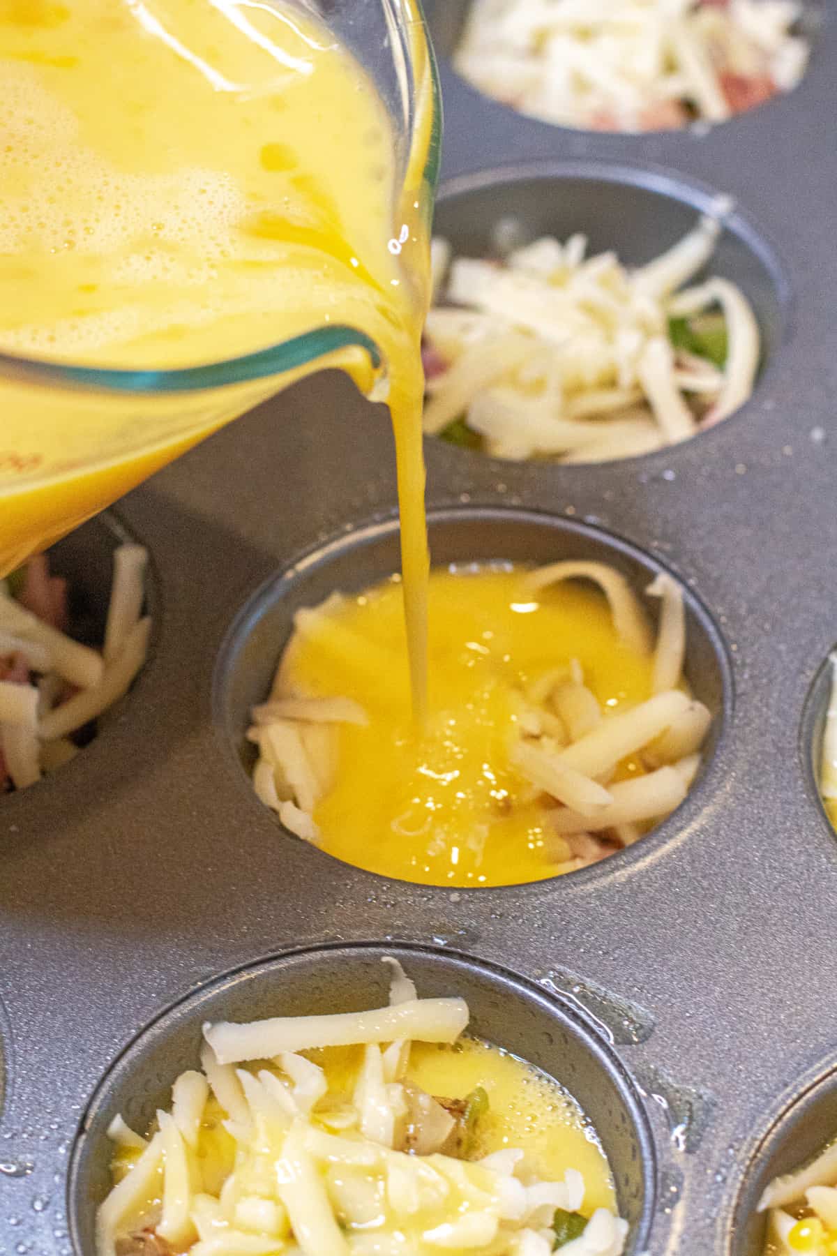 eggs being poured into cheese filled egg cups.
