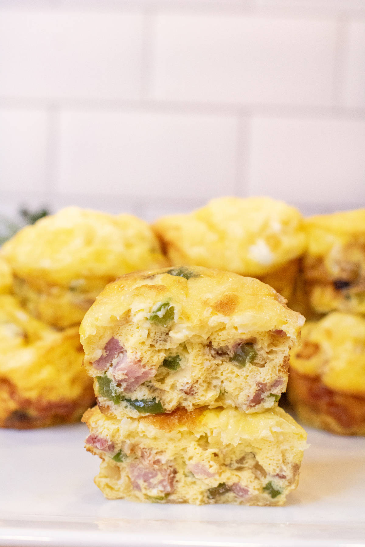 two halves of egg cups stuffed with ham, peppers, and onion stacked on a plate of other egg cups.