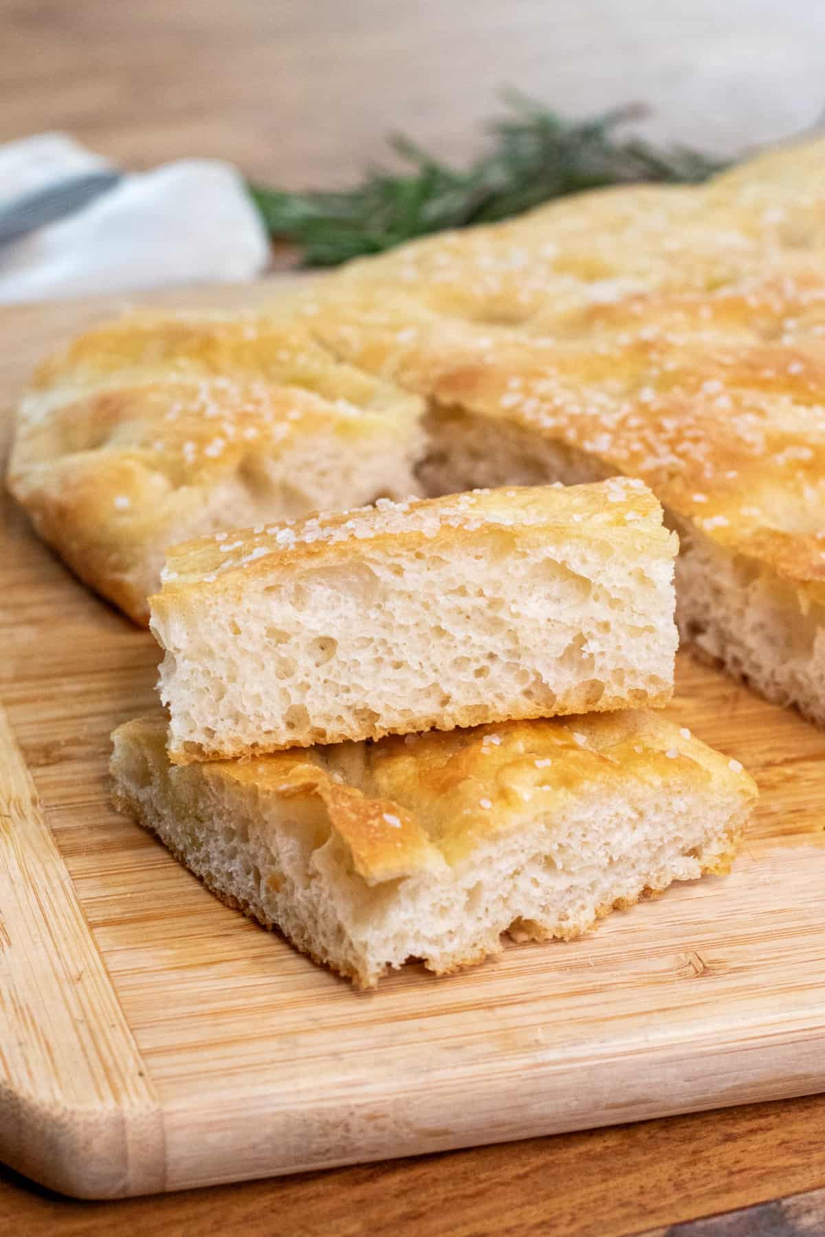 two pieces of stacked cut focaccia on a cutting board with the loaf.