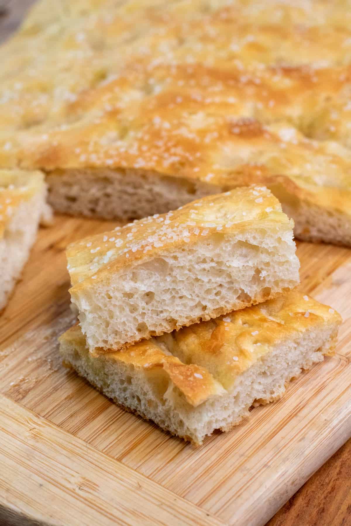 two pieces of stacked cut focaccia on a cutting board with the loaf.