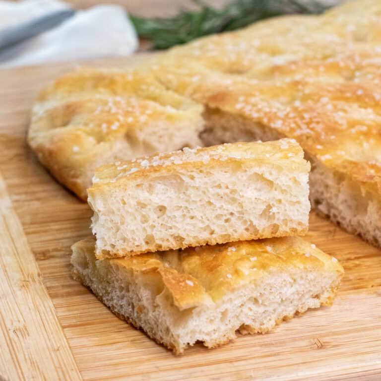 two pieces of stacked cut focaccia on a cutting board with the loaf.