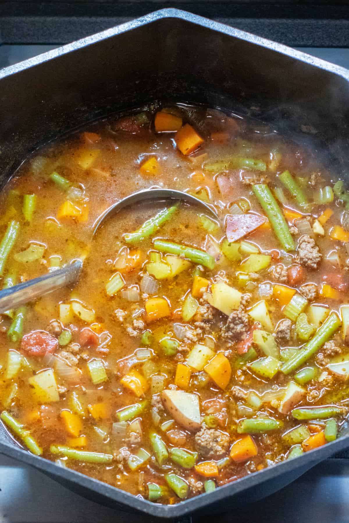 a dutch oven of beef and vegetable soup with a ladle in it.