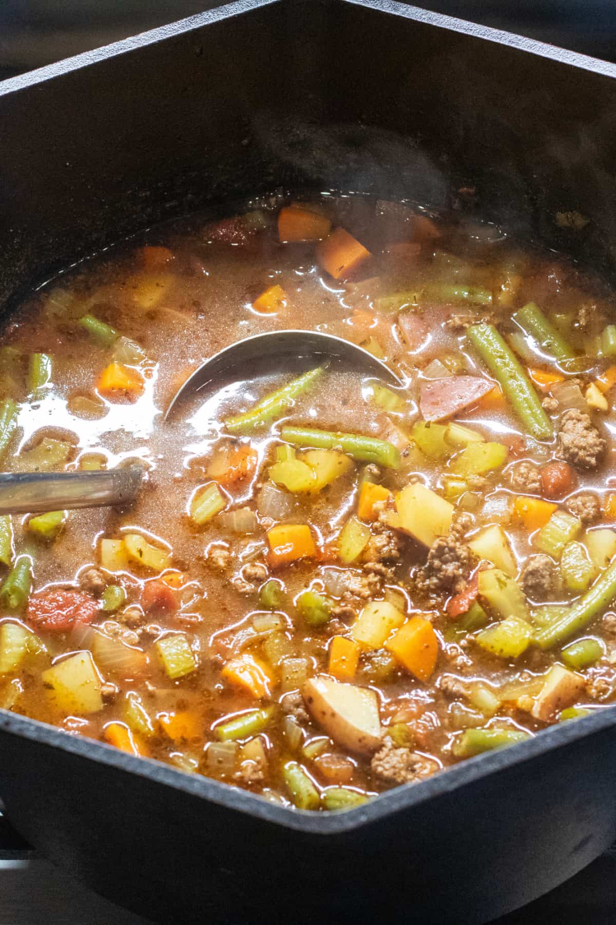 a dutch oven of beef and vegetable soup with a ladle in it.