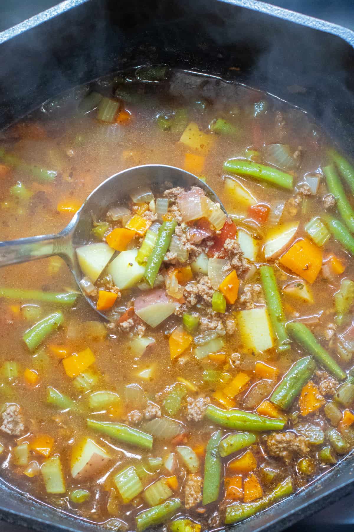 a dutch oven of beef and vegetable soup with a ladle in it.
