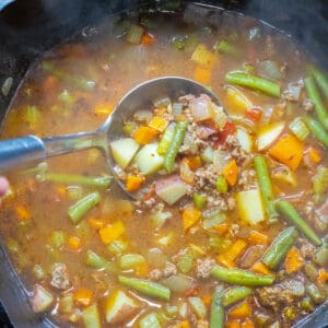 a dutch oven of beef and vegetable soup with a ladle in it.