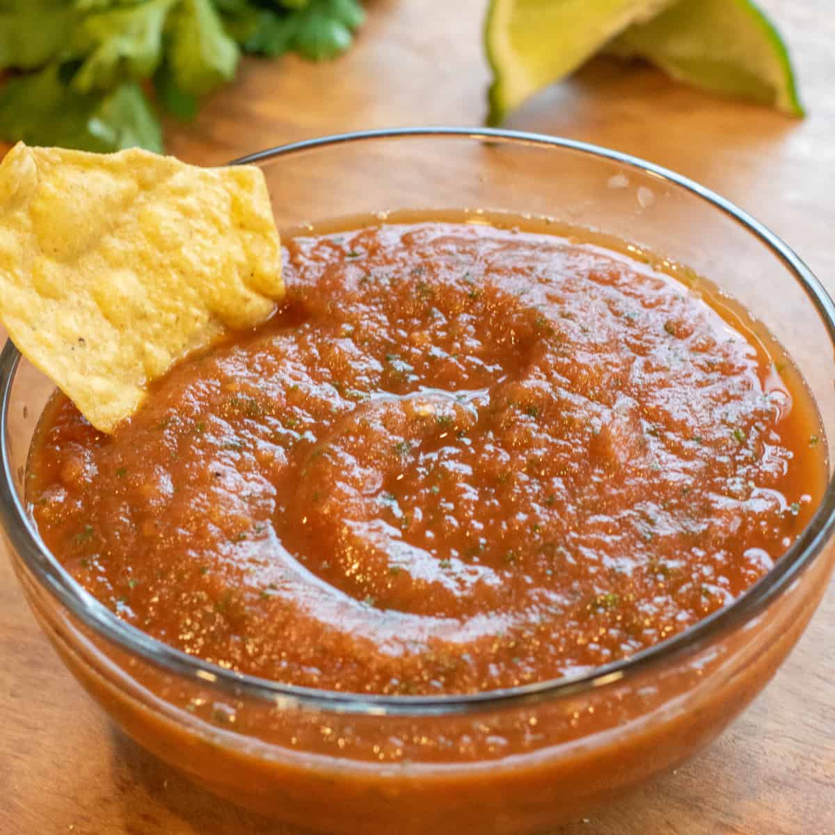 a bowl of smooth tomato salsa with a chip in it.