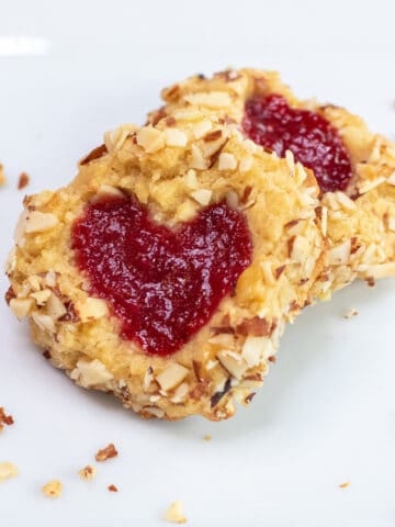 a plate with two cookies with heart jam and coated in almonds.