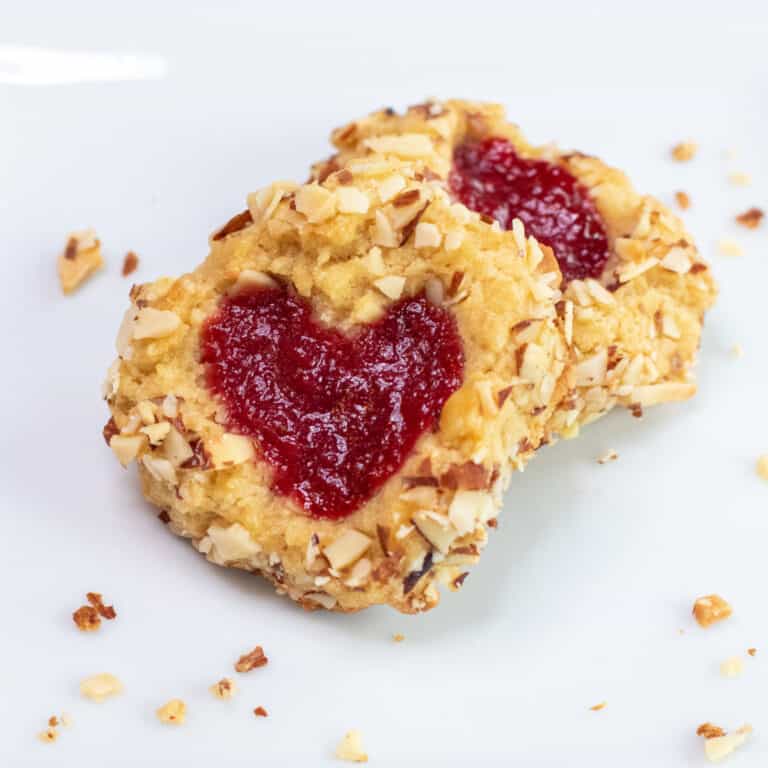 a plate with two cookies with heart jam and coated in almonds.