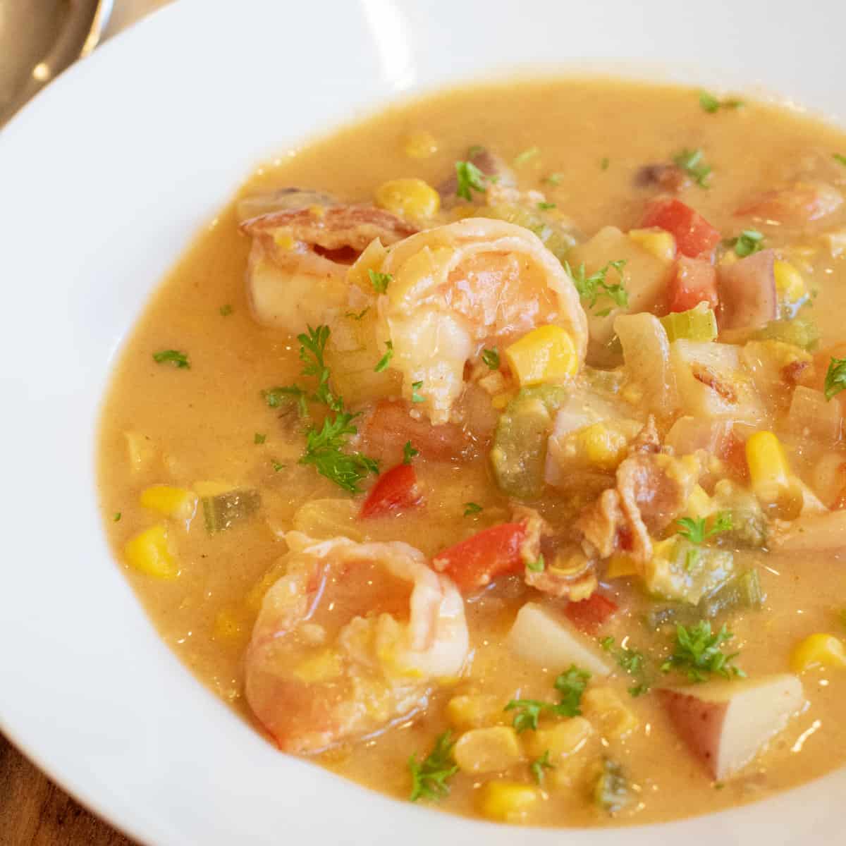 a bowl of shrimp chowder with corn red pepper and potatoes.