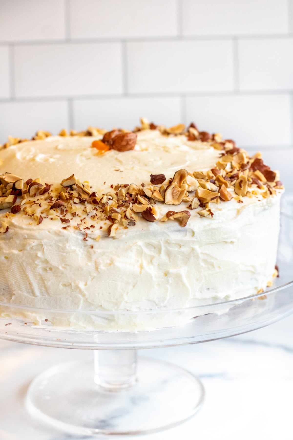 a frosted cake with hazelnuts on top on a cake stand. 