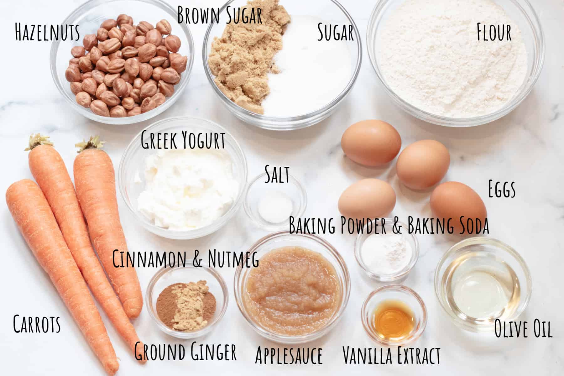 bowls of hazelnuts, flour, sugar, whole carrots, eggs, yogurt, applesauce, spices.