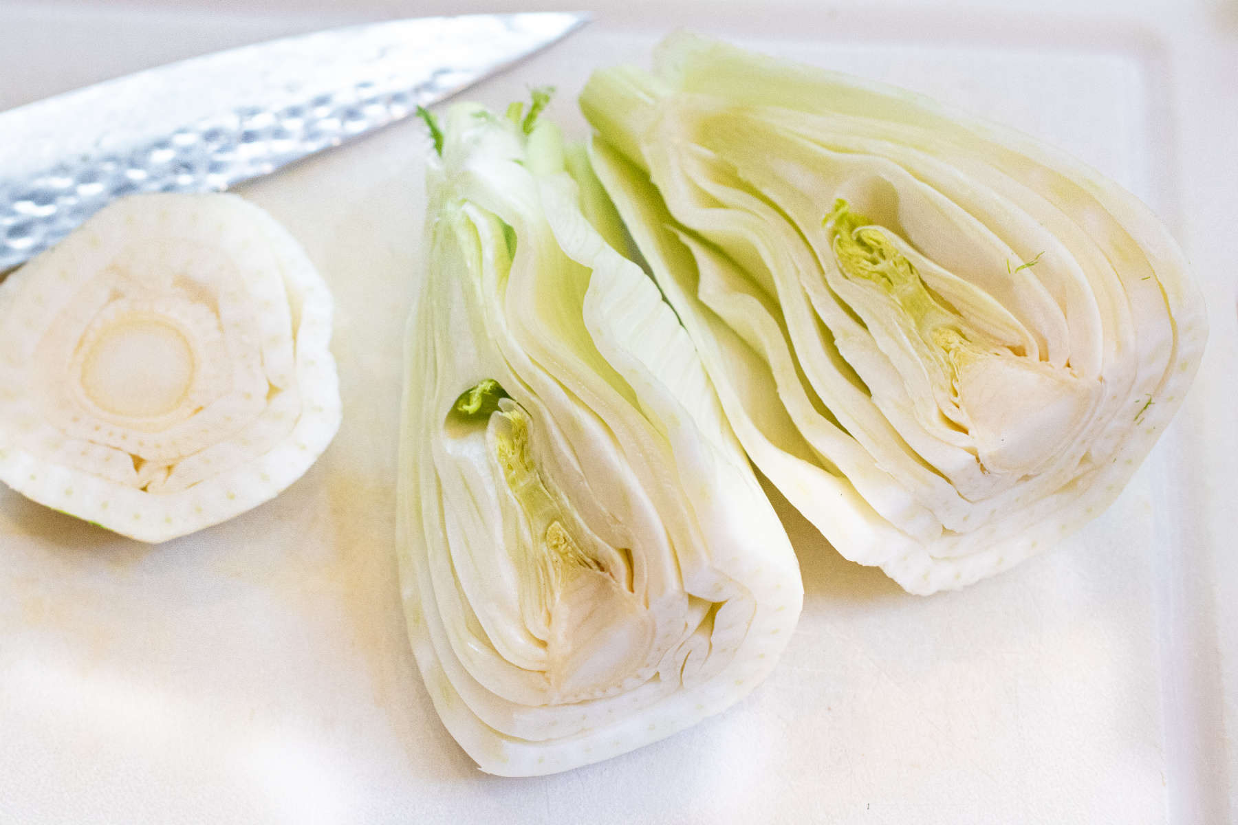a fennel halved on a cutting board with a knife.