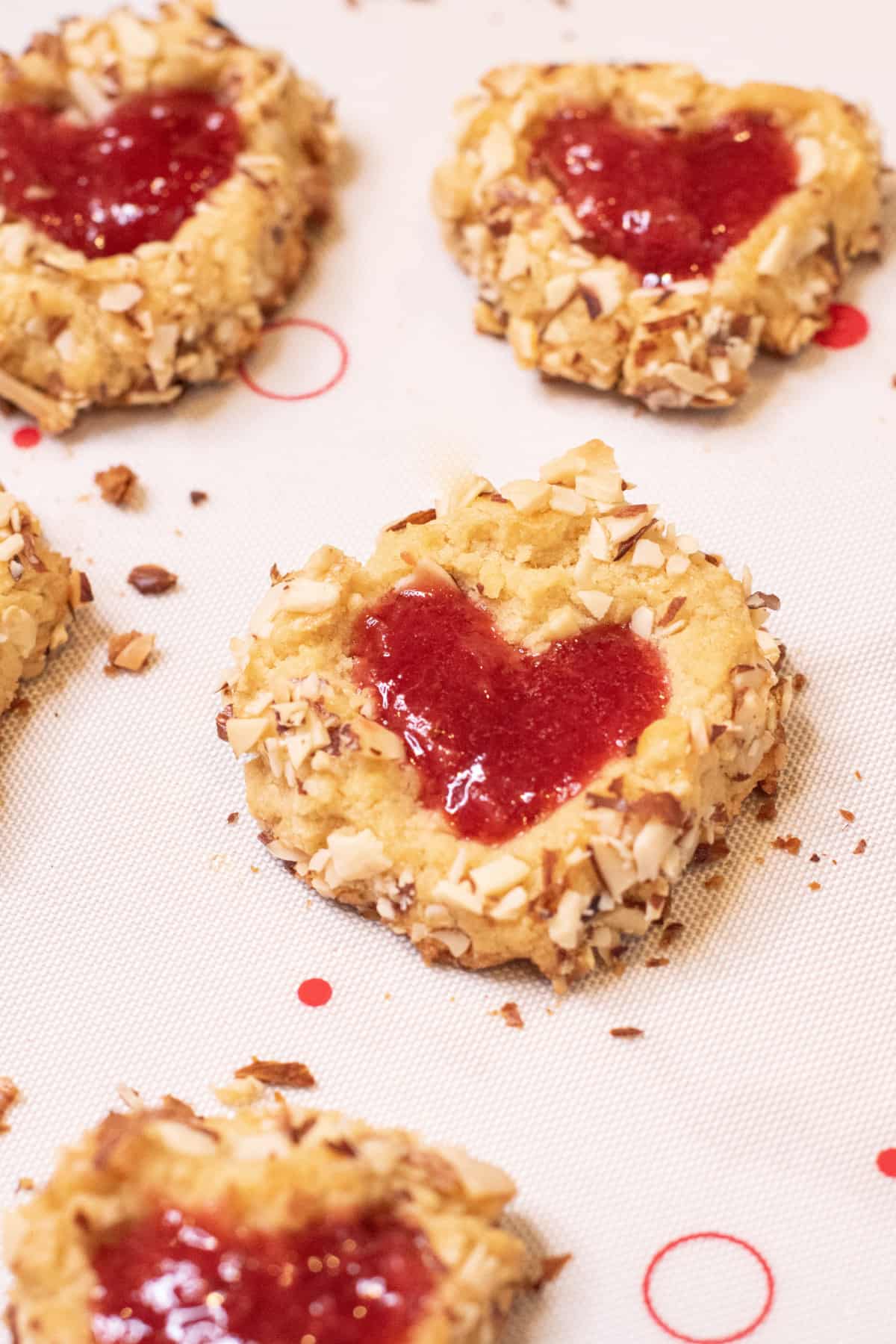 heart filled jam thumbprint cookies on a baking mat.