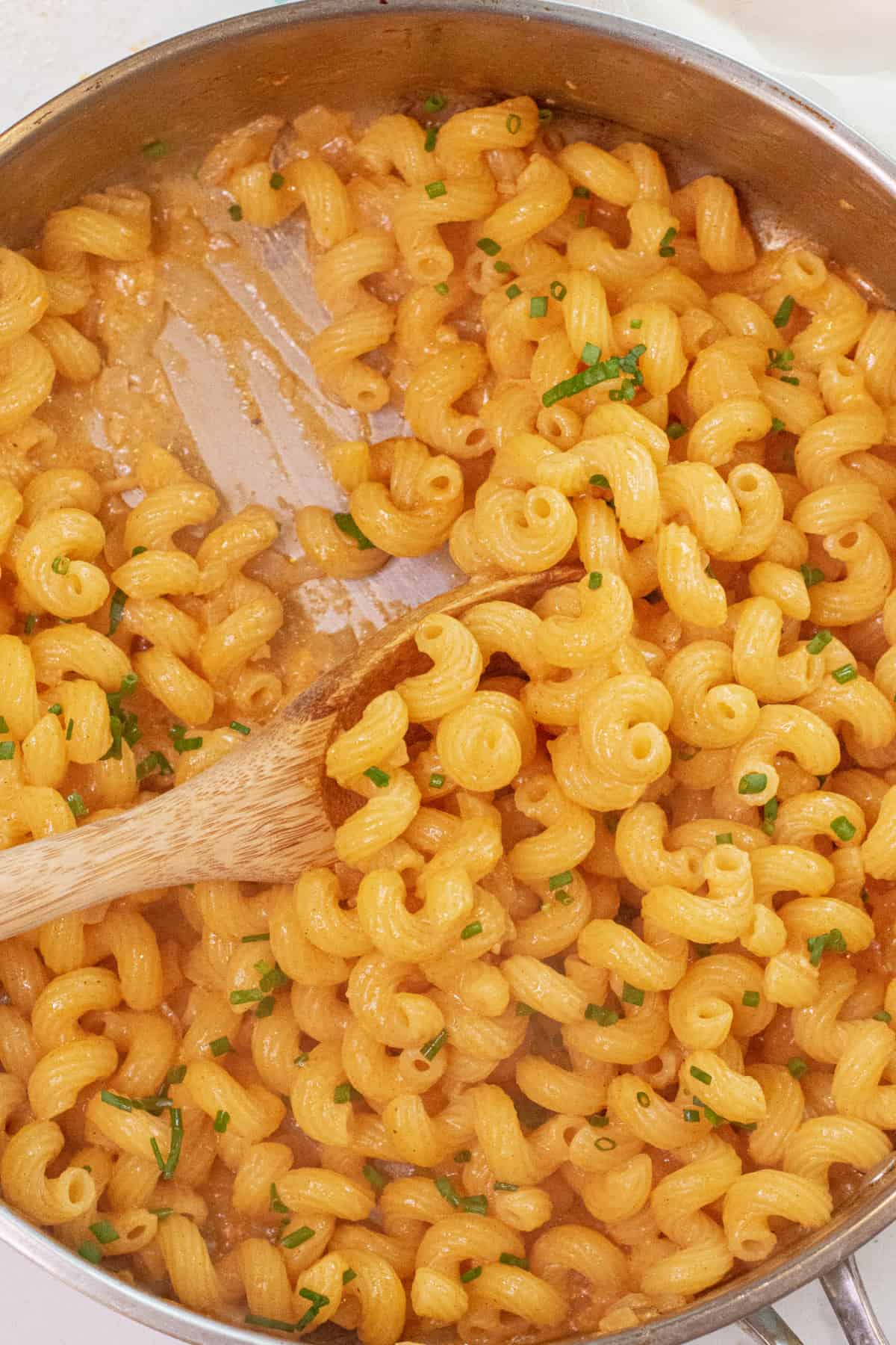 a pan of cooked pasta in a creamy sauce with a wooden spoon.