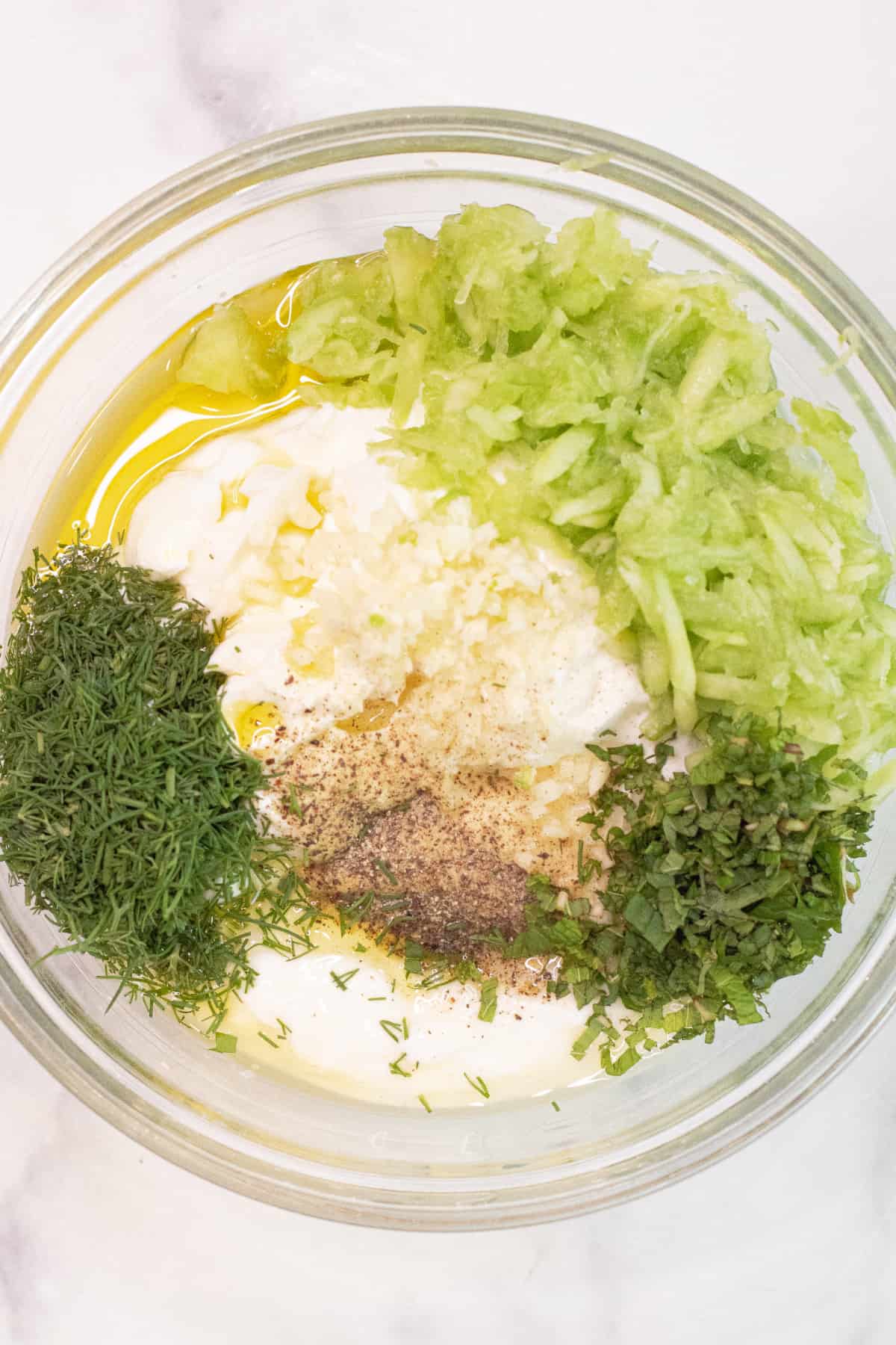 a bowl of yogurt with fresh herbs, shredded cucumber, salt and pepper, and olive oil.