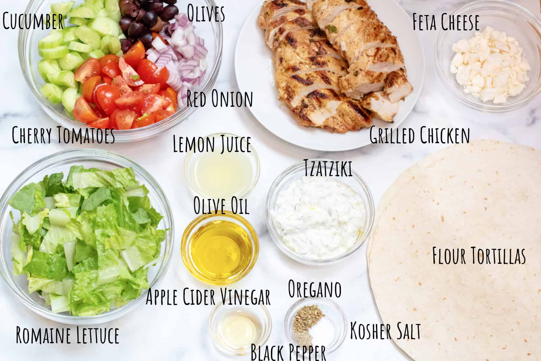 grilled sliced chicken on a plate, a bowl of cucumber, olives, tomatoes, onions, lettuce, oil, tzatziki, tortillas, salt and pepper in bowls and labeled.