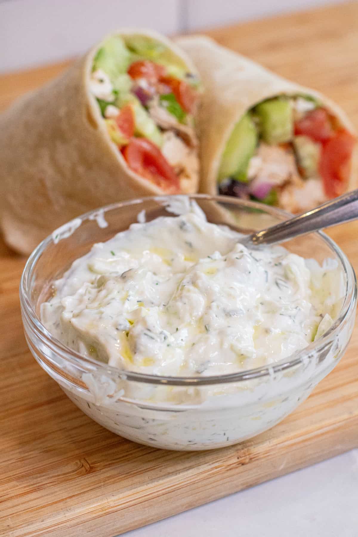 a bowl of tzatziki in front of a halved wrap on a cutting board.