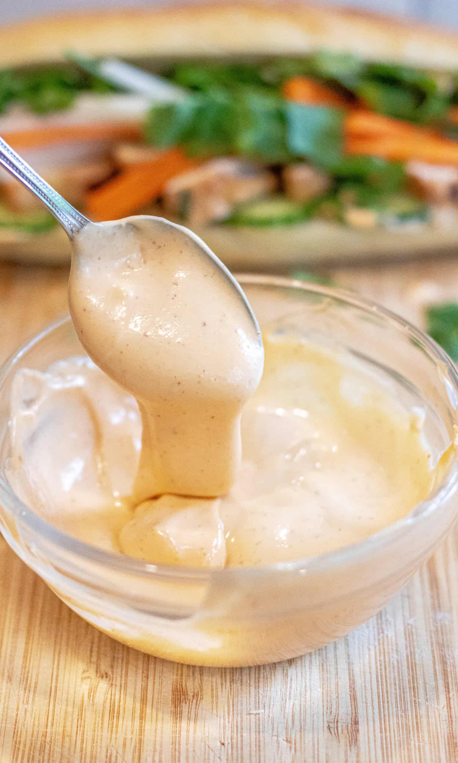 a bowl of sriracha mayo with a spoon taking some out and a sandwich in the back.