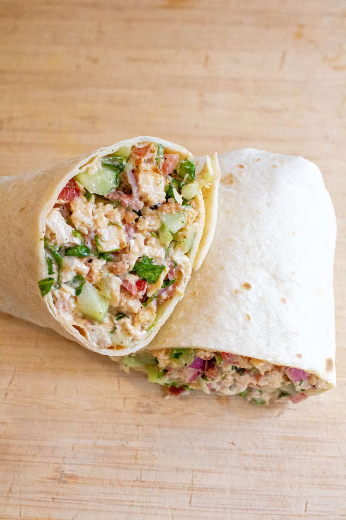 a halved sandwich wrap stuffed with greens and chicken and bacon.