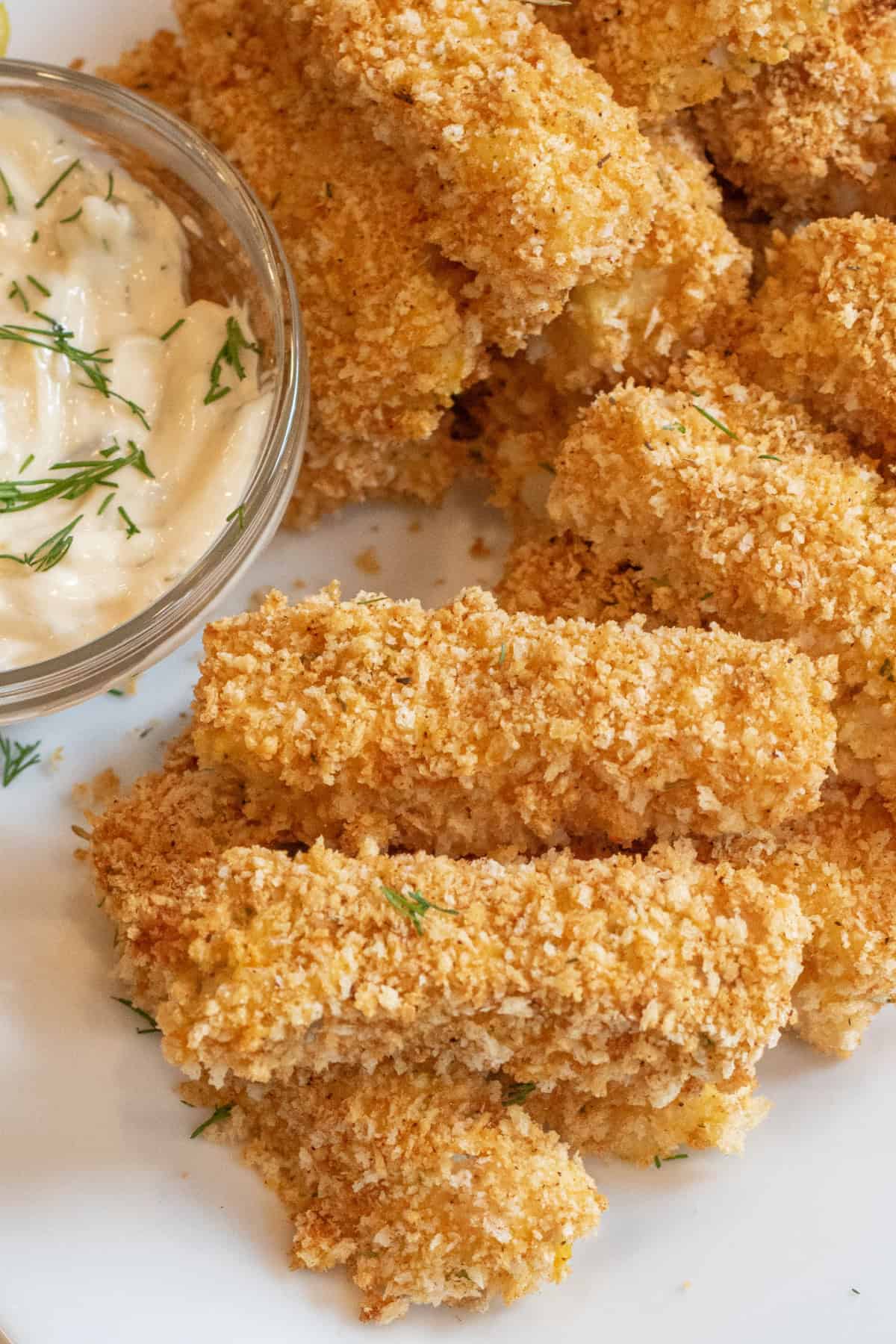 baked breaded fish sticks stacked on a plate.