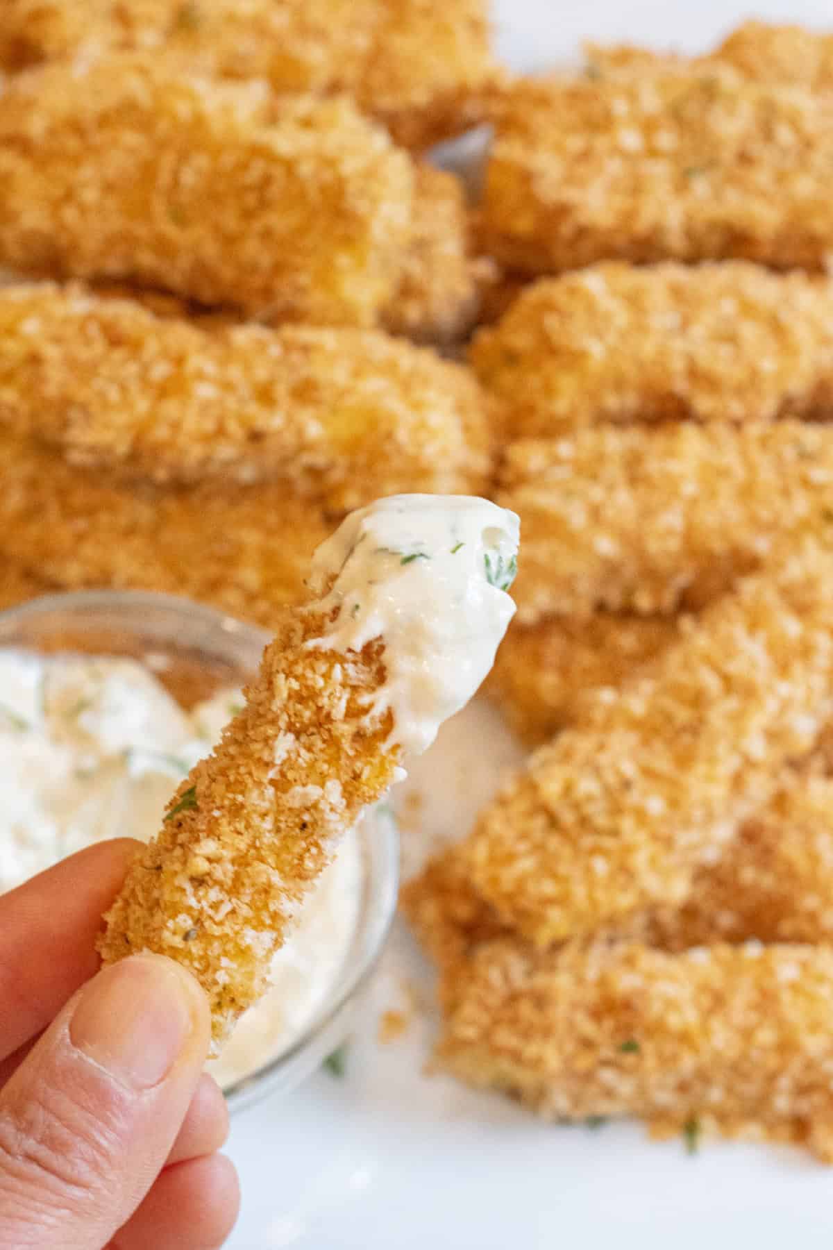 a hand holding a breaded fish sticks dipped in tartar sauce.