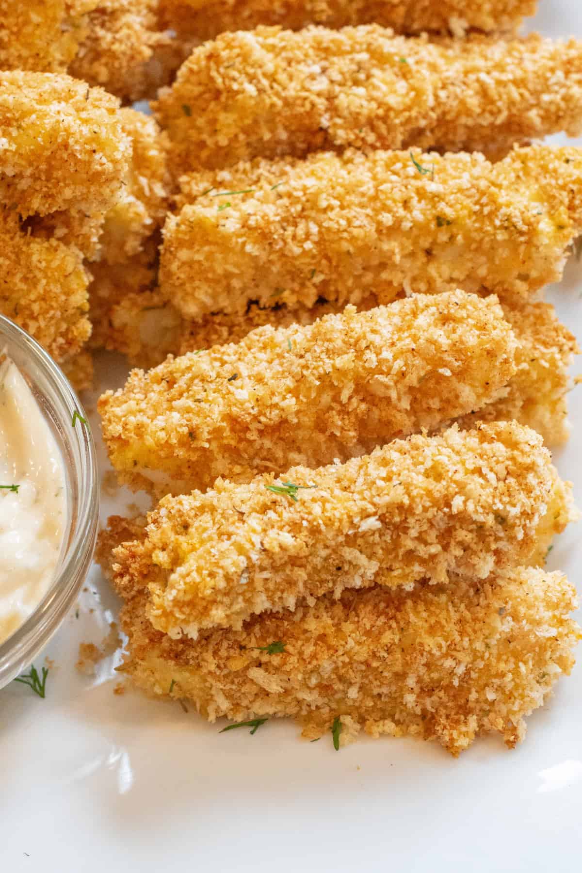 baked breaded fish sticks stacked on a plate.