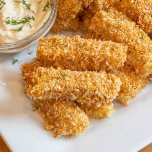 baked breaded fish sticks stacked on a plate.