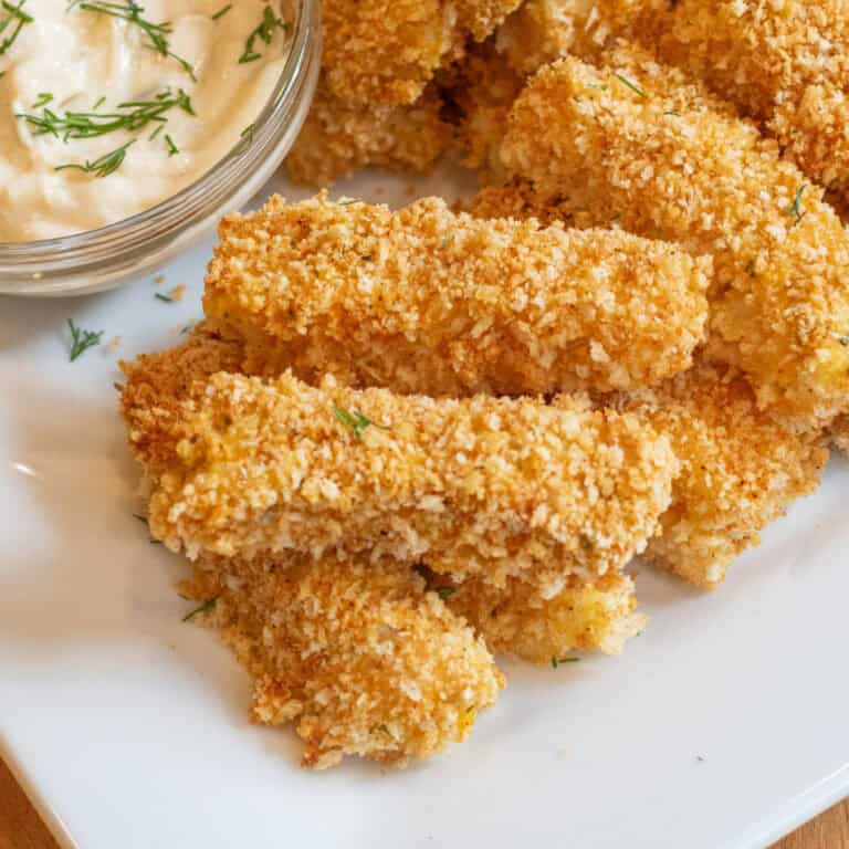 baked breaded fish sticks stacked on a plate.