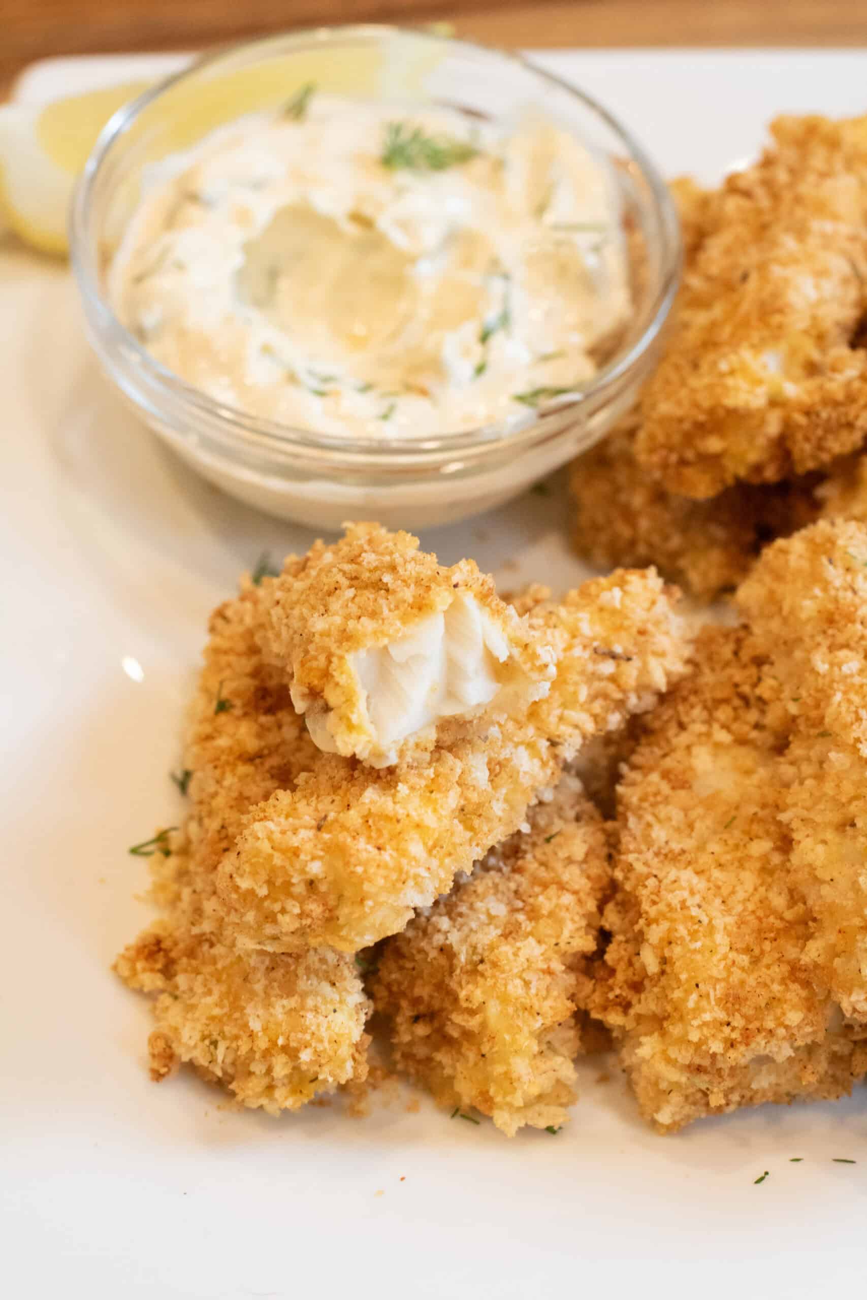 baked breaded fish sticks stacked on a plate with one open.