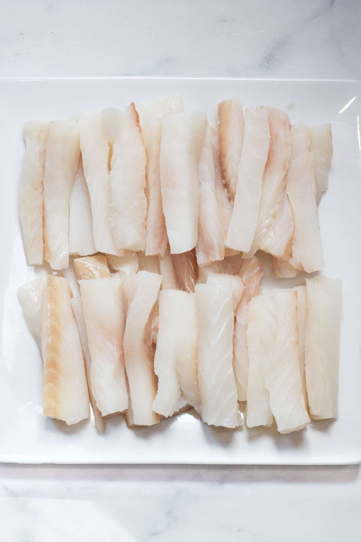 a plate of cut cod in sticks on a plate.