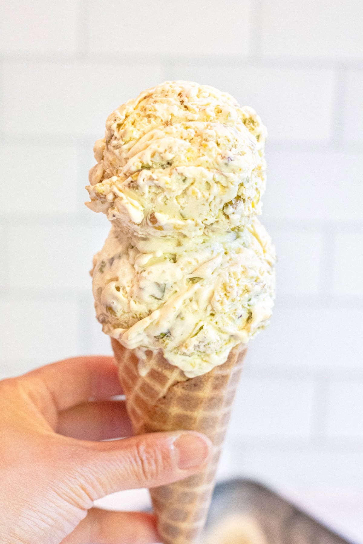 a hand holding an ice cream cone with two scoops of pistachio ice cream.