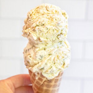 a hand holding a two scoop ice cream cone of pistachio ice cream.