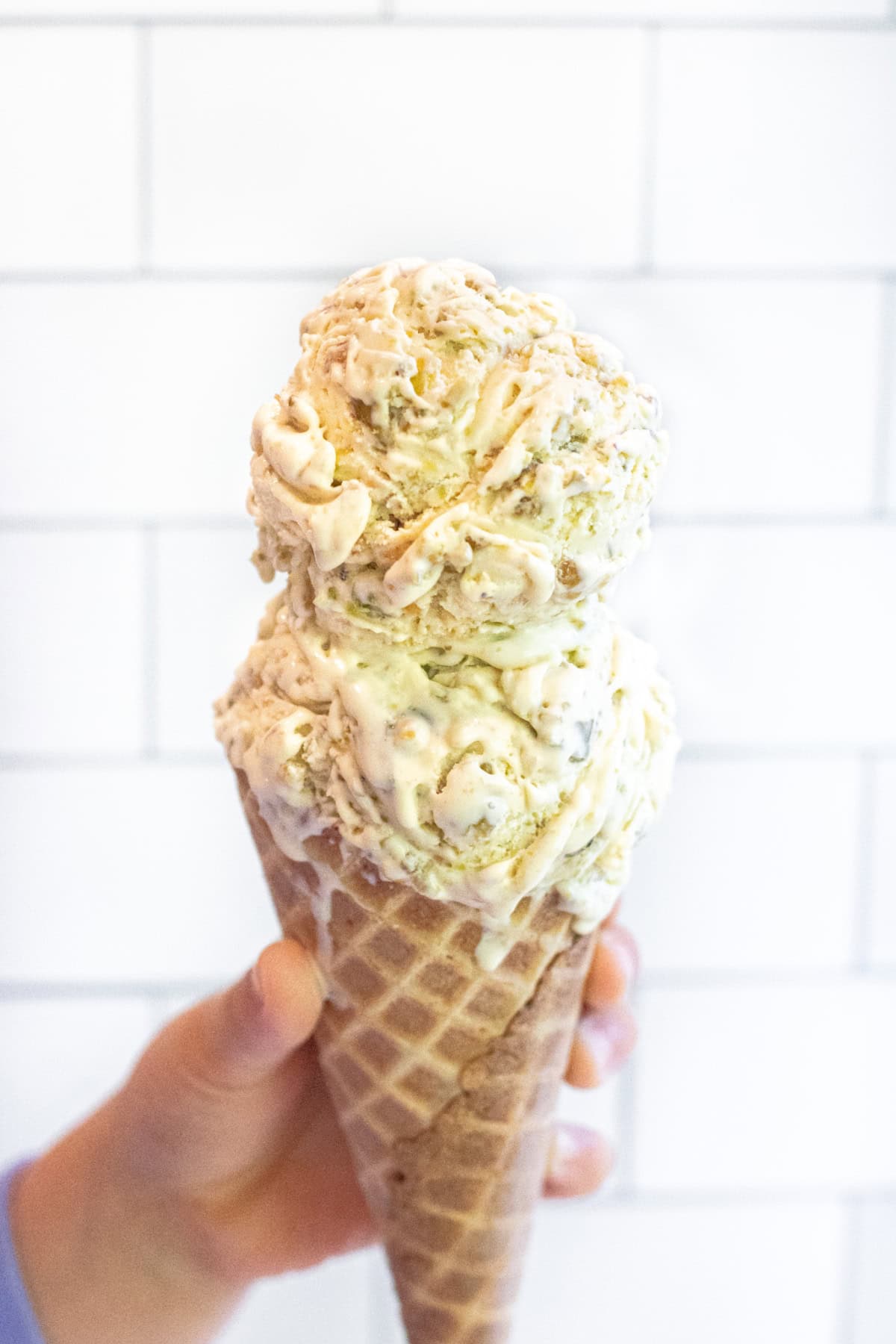 a hand holding a two scoop ice cream cone of pistachio ice cream.