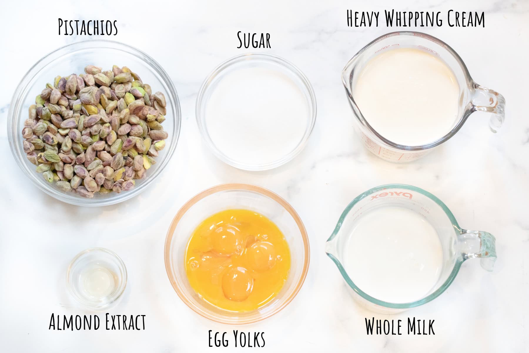 a bowl of pistachios, sugar, cream, milk, egg yolks, and almond extract in bowls and labeled. 