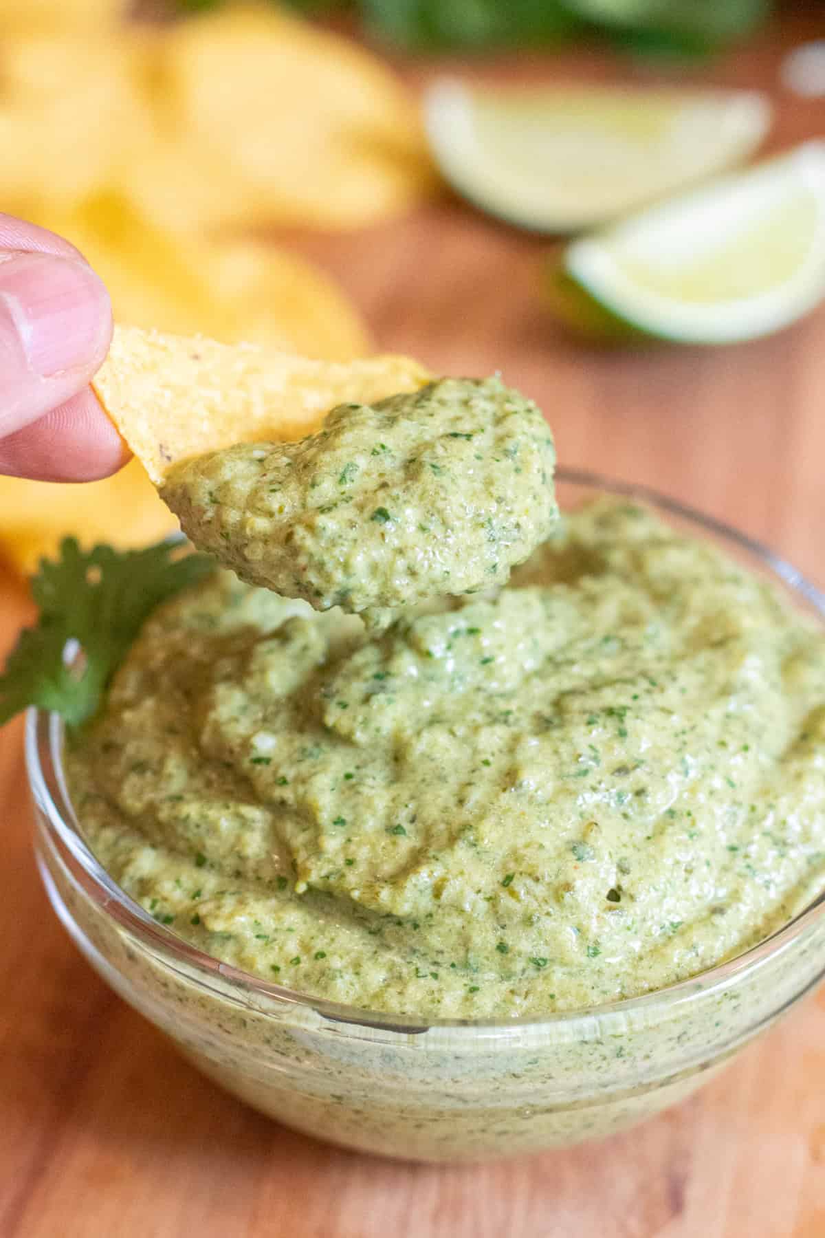 a bowl of poblano sauce and a chip being held up with the sauce.