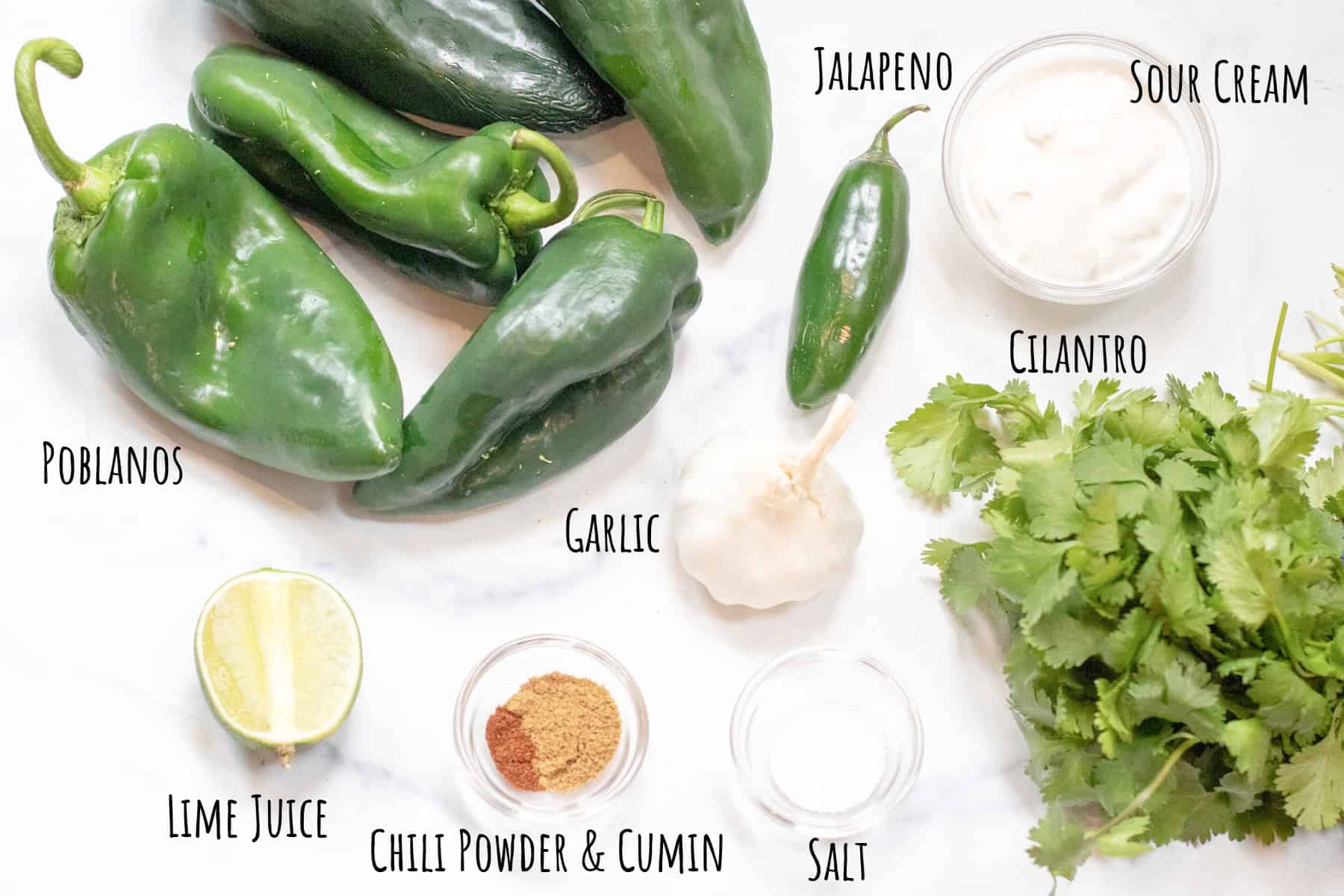 poblanos, jalapeno, sour cream, lime, spices, garlic, and cilantro on a table and labeled.