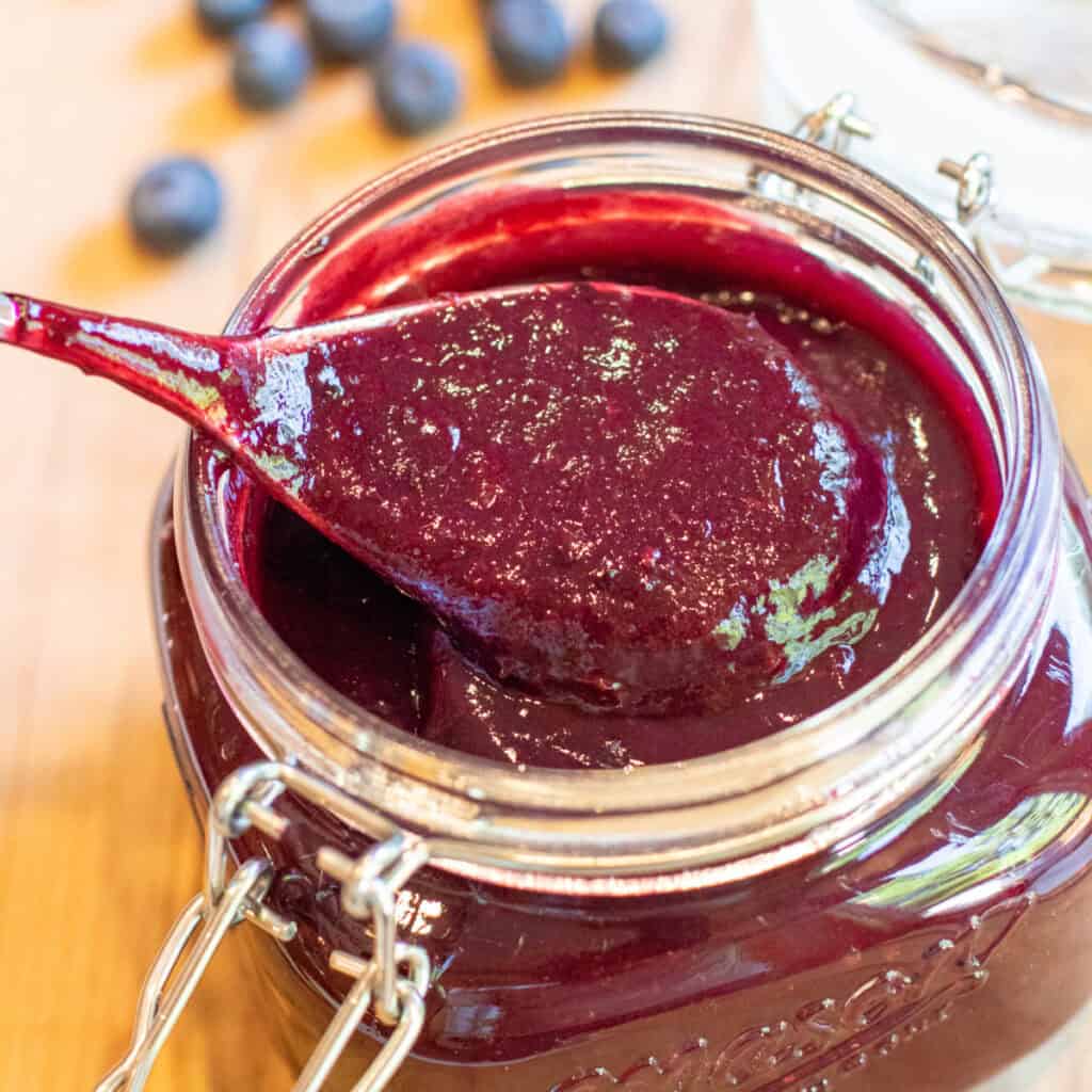 an open mason jar with a spoon and blueberry bbq sauce.