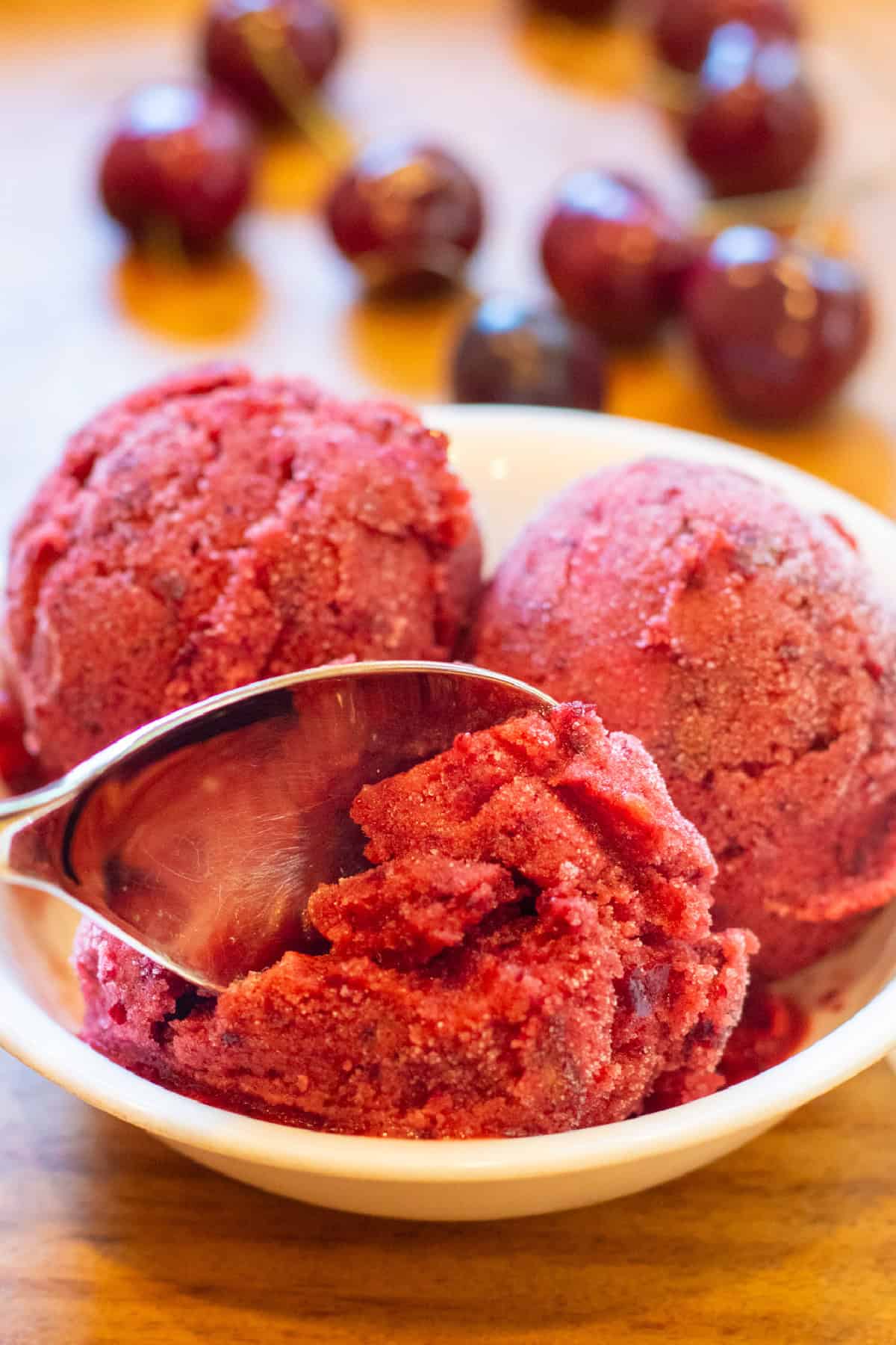 a bowl of 3 scoops of cherry sorbet and with a spoon.