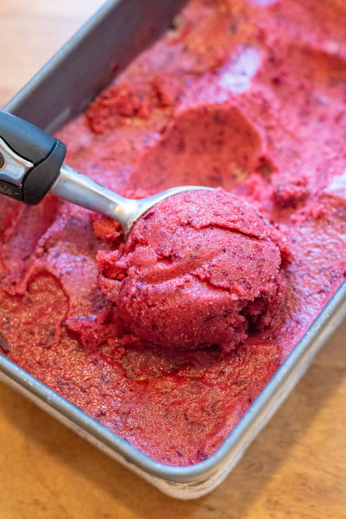 an ice cream scoop, scooping cherry sorbet from a loaf pan.