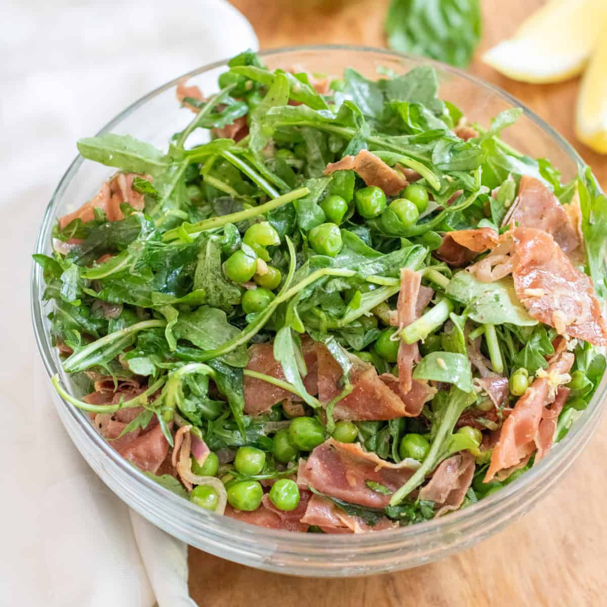 a bowl of salad with peas, prosciutto, and arugula.