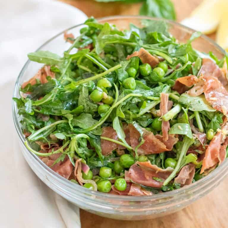 a bowl of salad with peas, prosciutto, and arugula.