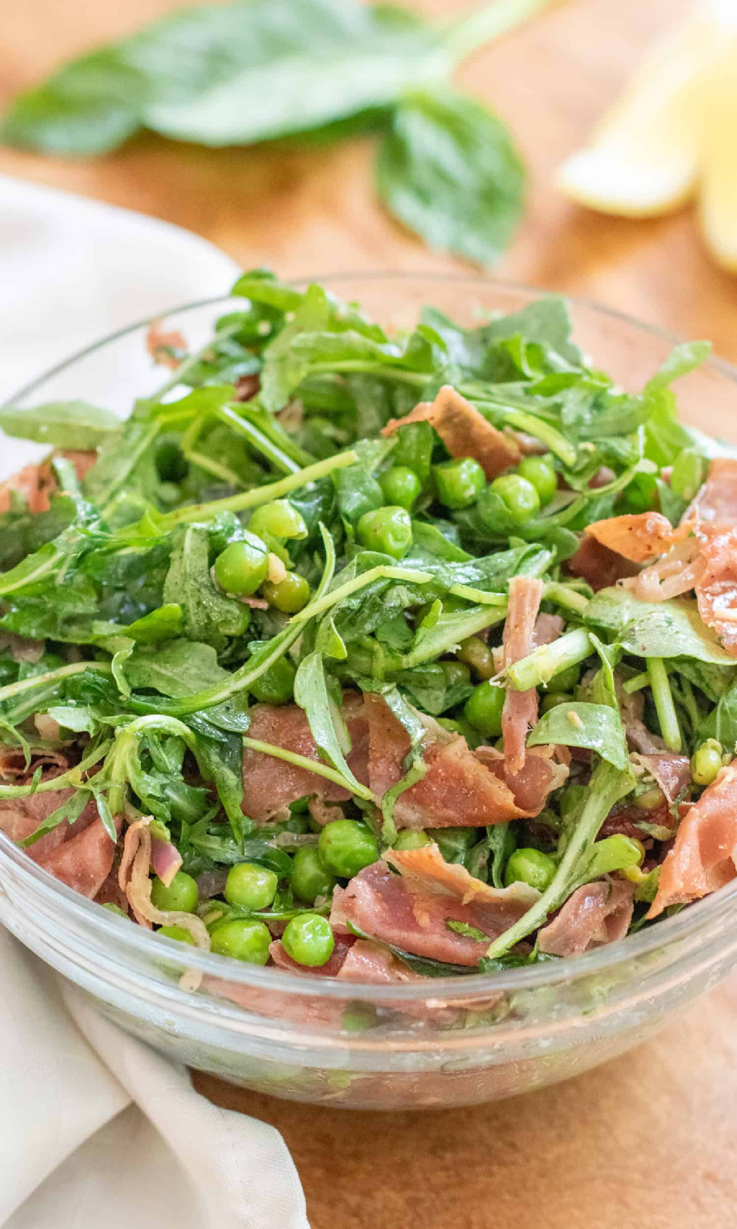 a bowl of salad with peas, prosciutto, and arugula.