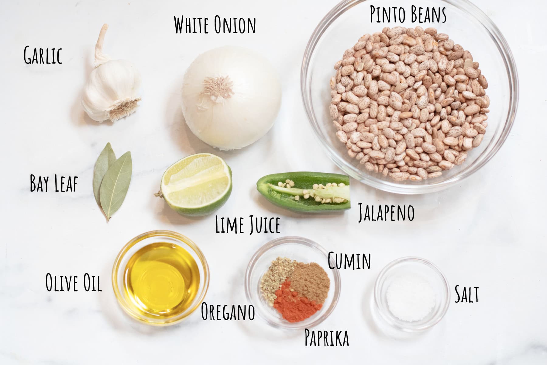 a bowl of pinto beans, a white onion, garlic, jalapeno, oil, spices, salt, garlic, bay leaves, and half a lime.