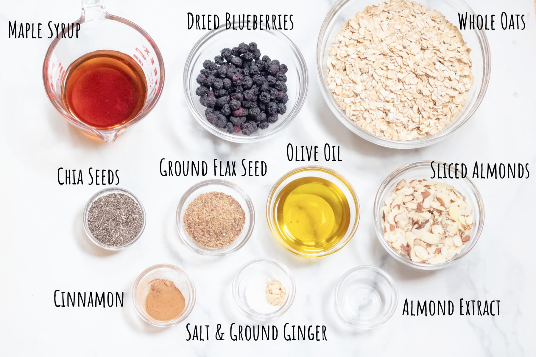 labeled maple syrup, oats, dried blueberries, chia seeds, ground flax, olive oil, sliced almonds, cinnamon, salt, ground ginger, and almond extract.