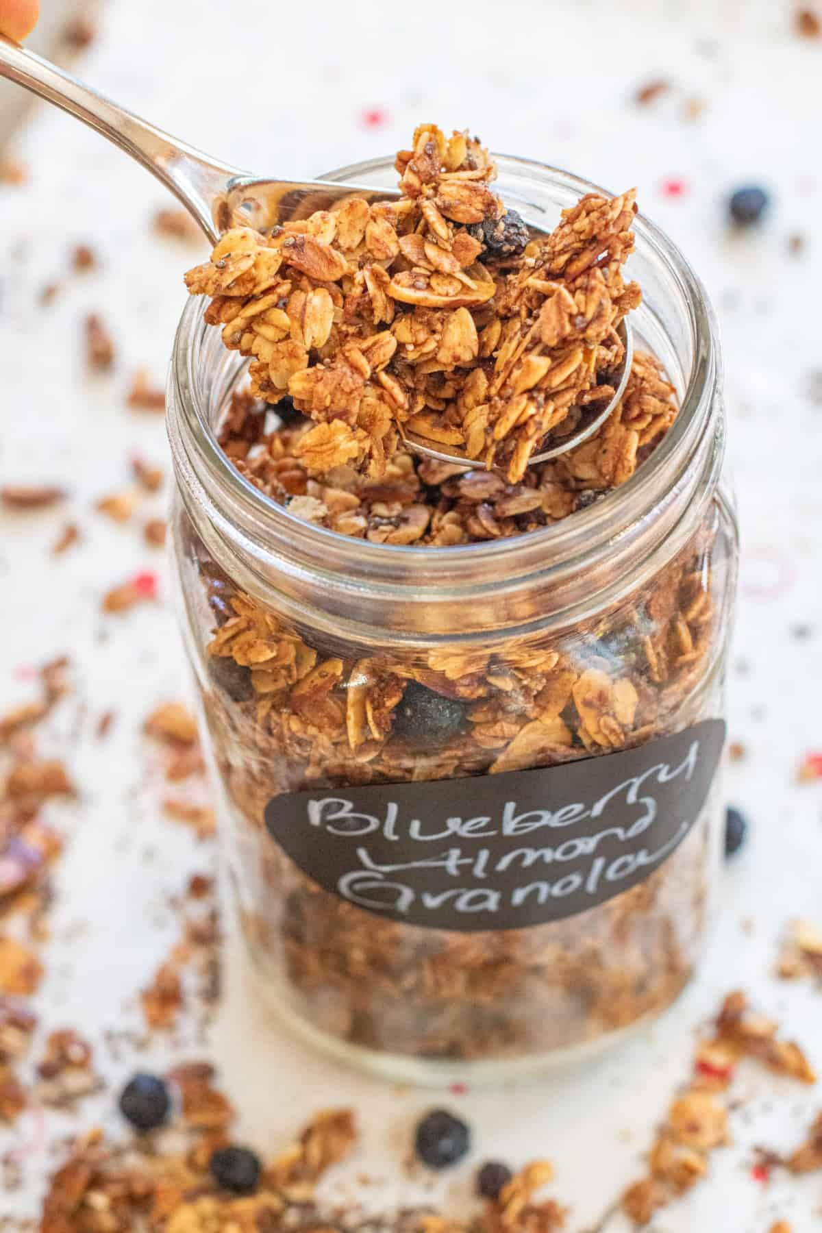 a jar of labeled blueberry almond granola with a spoon taking some out.