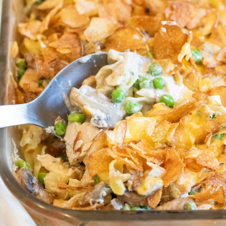 a spoon in a casserole with potato chips and peas, mushrooms, noodles, and tuna.