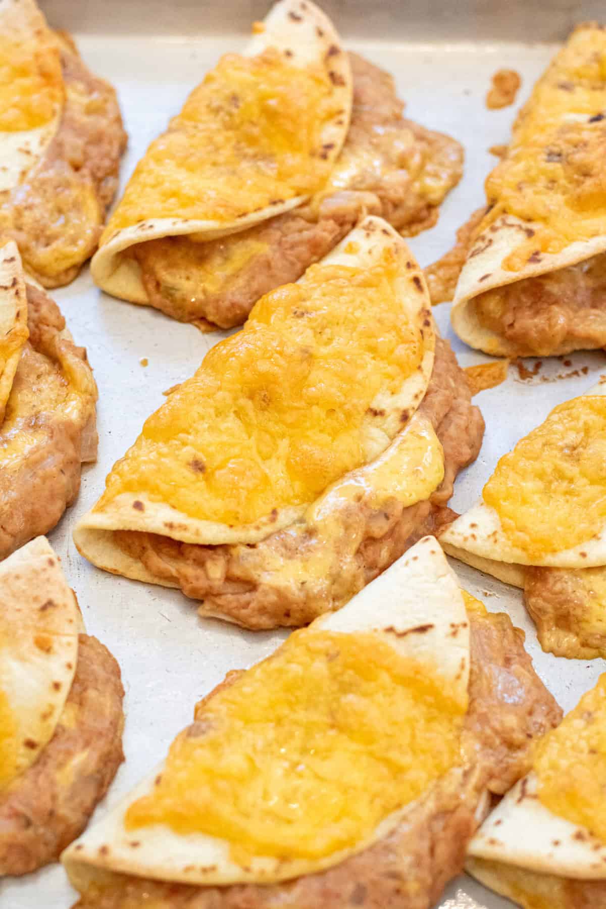 a tray of baked crispy tacos with beans and cheese.