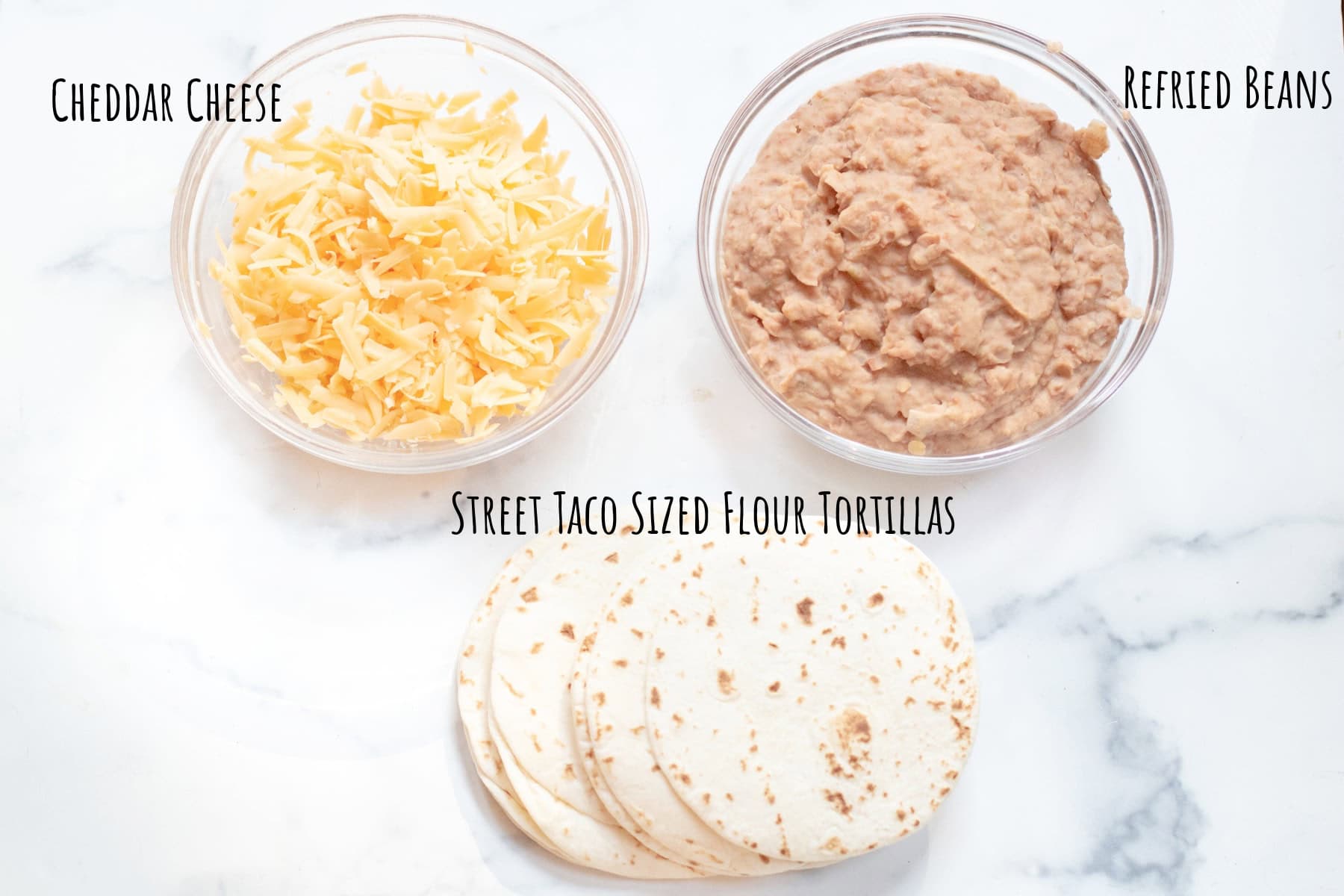 bowls of shredded cheese and refried beans and flour tortillas labeled.